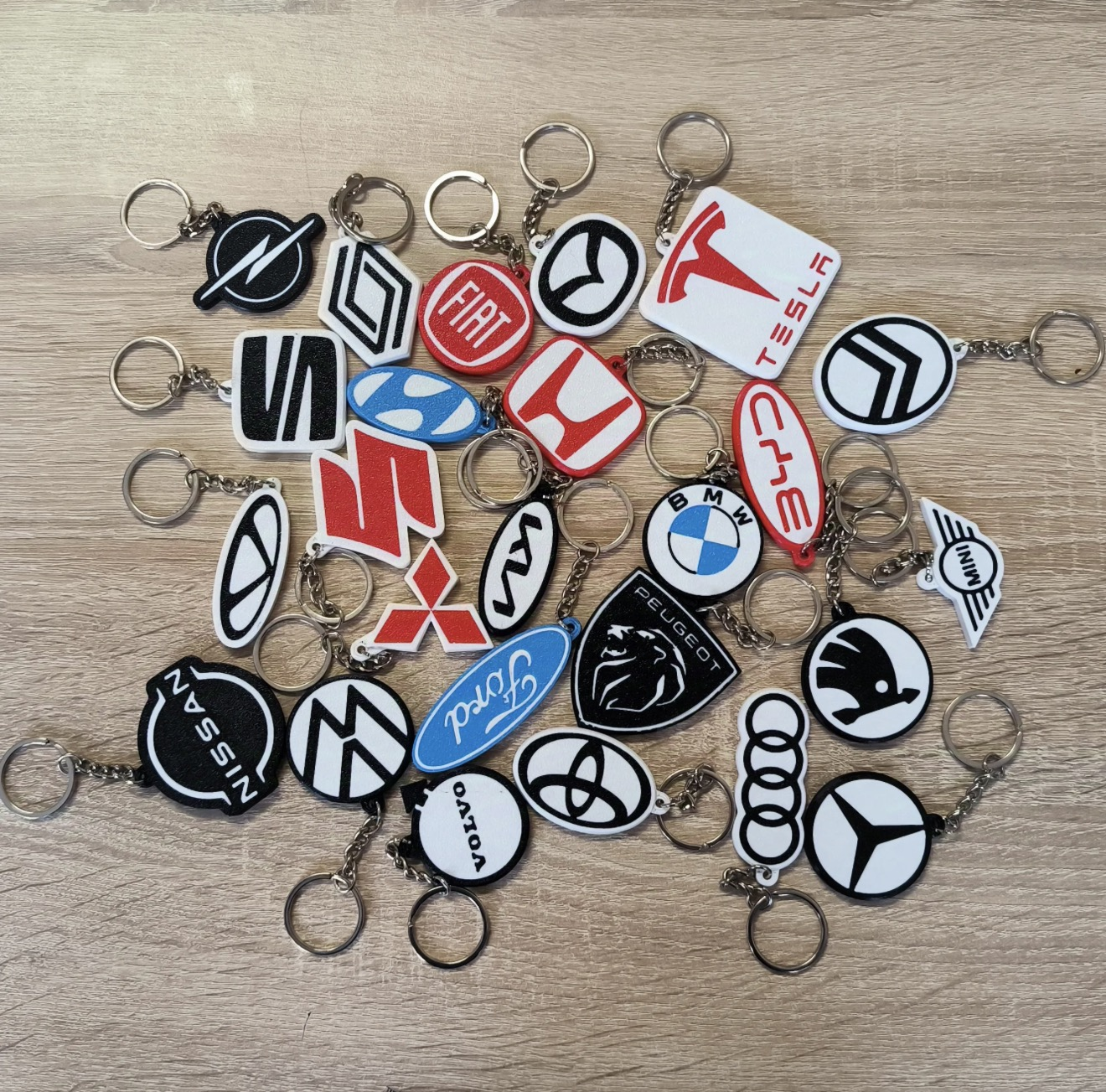 Assorted custom 3D printed automotive-style logo keychains with metal key rings.