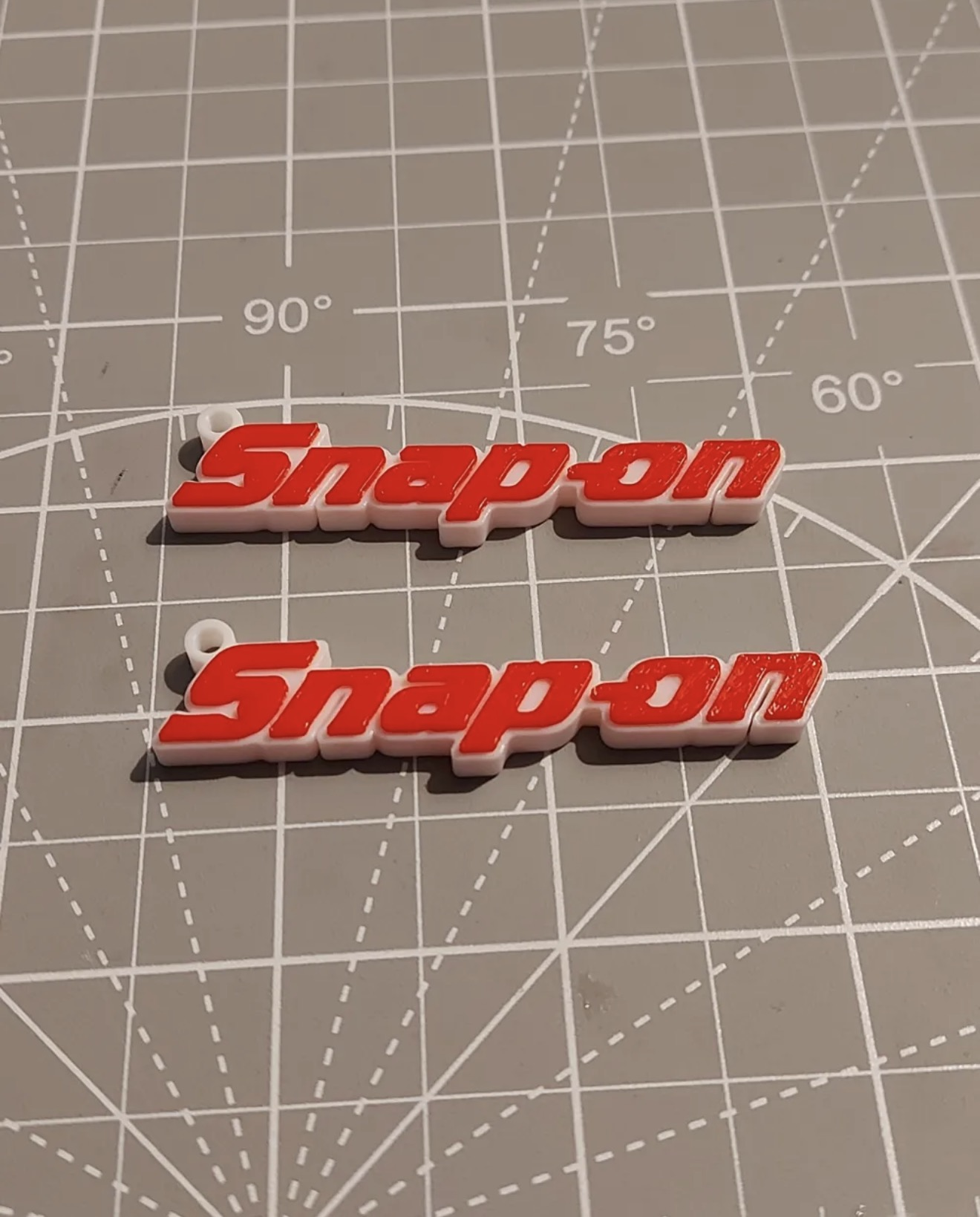 Custom red and white 3D printed wordmark-style keychains on a cutting mat.