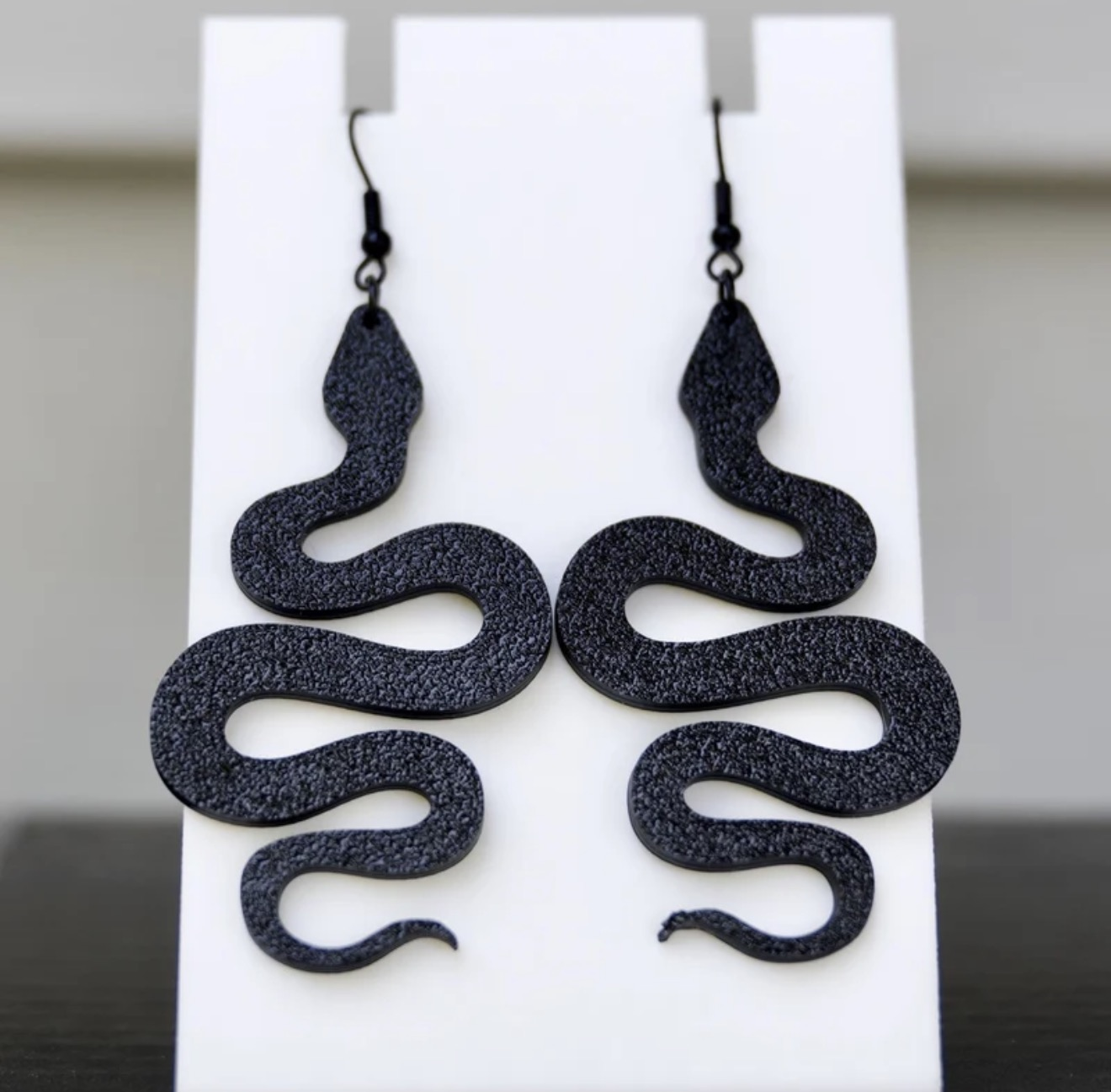Black 3D printed snake-shaped earrings displayed on a white jewelry stand.
