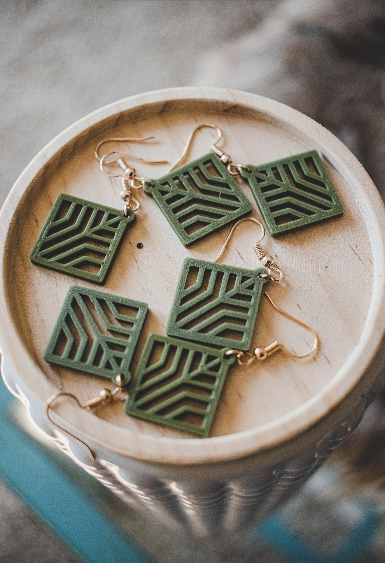 Green 3D printed geometric square earrings arranged on a wood display bowl.