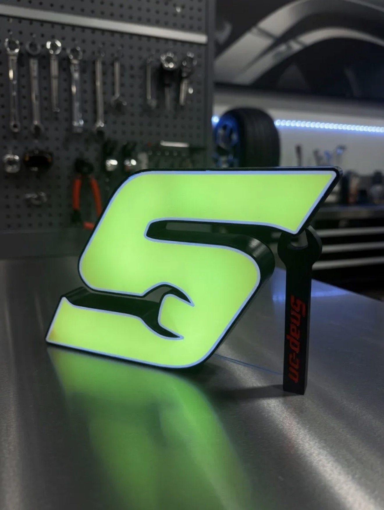 Custom illuminated green wrench-style logo lightbox sign on a workbench.