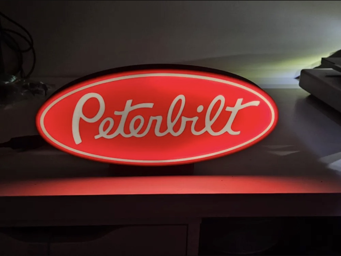 Custom red oval illuminated logo-style lightbox sign on a shelf.