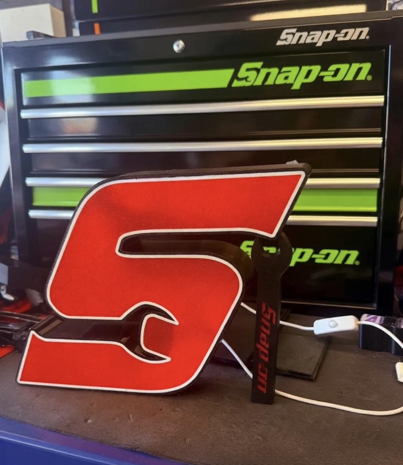 Custom red wrench-style logo lightbox sign in front of a tool chest.